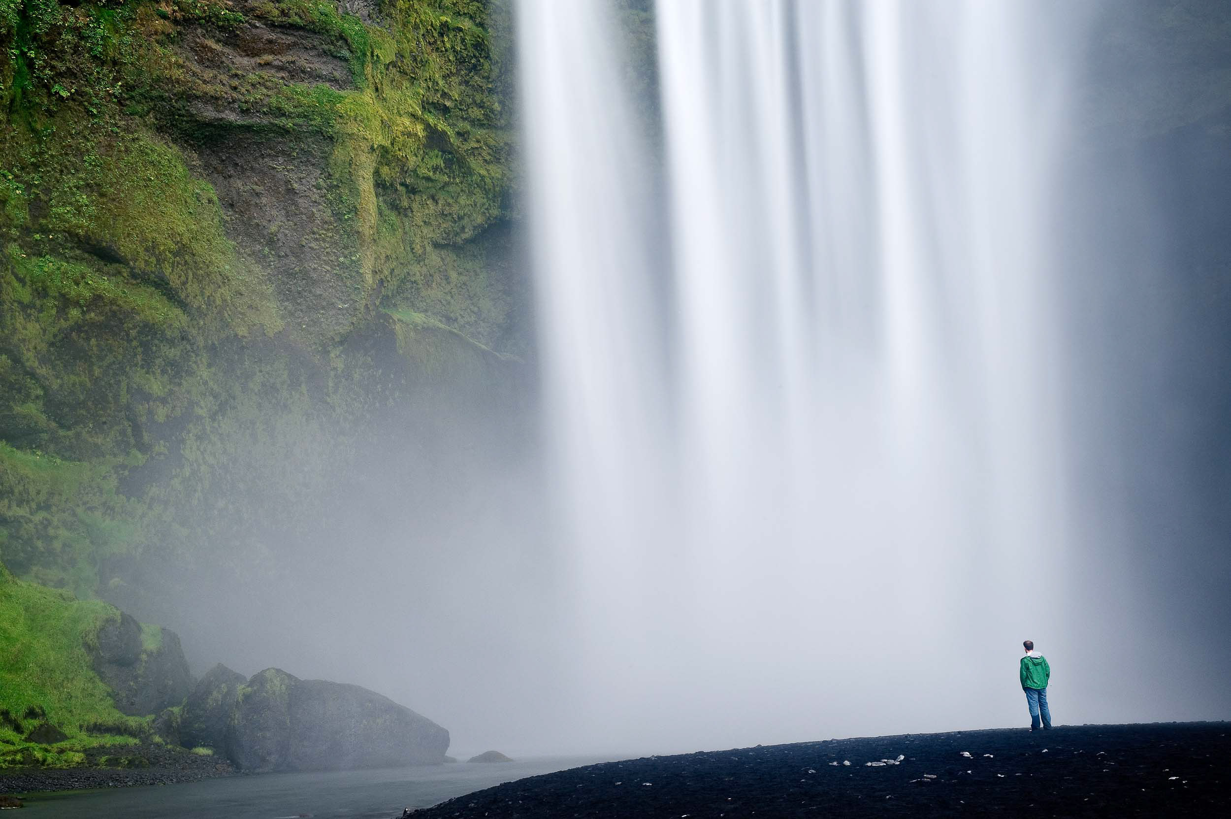 man-standing-below-skogar-waterfall-iceland-landscape